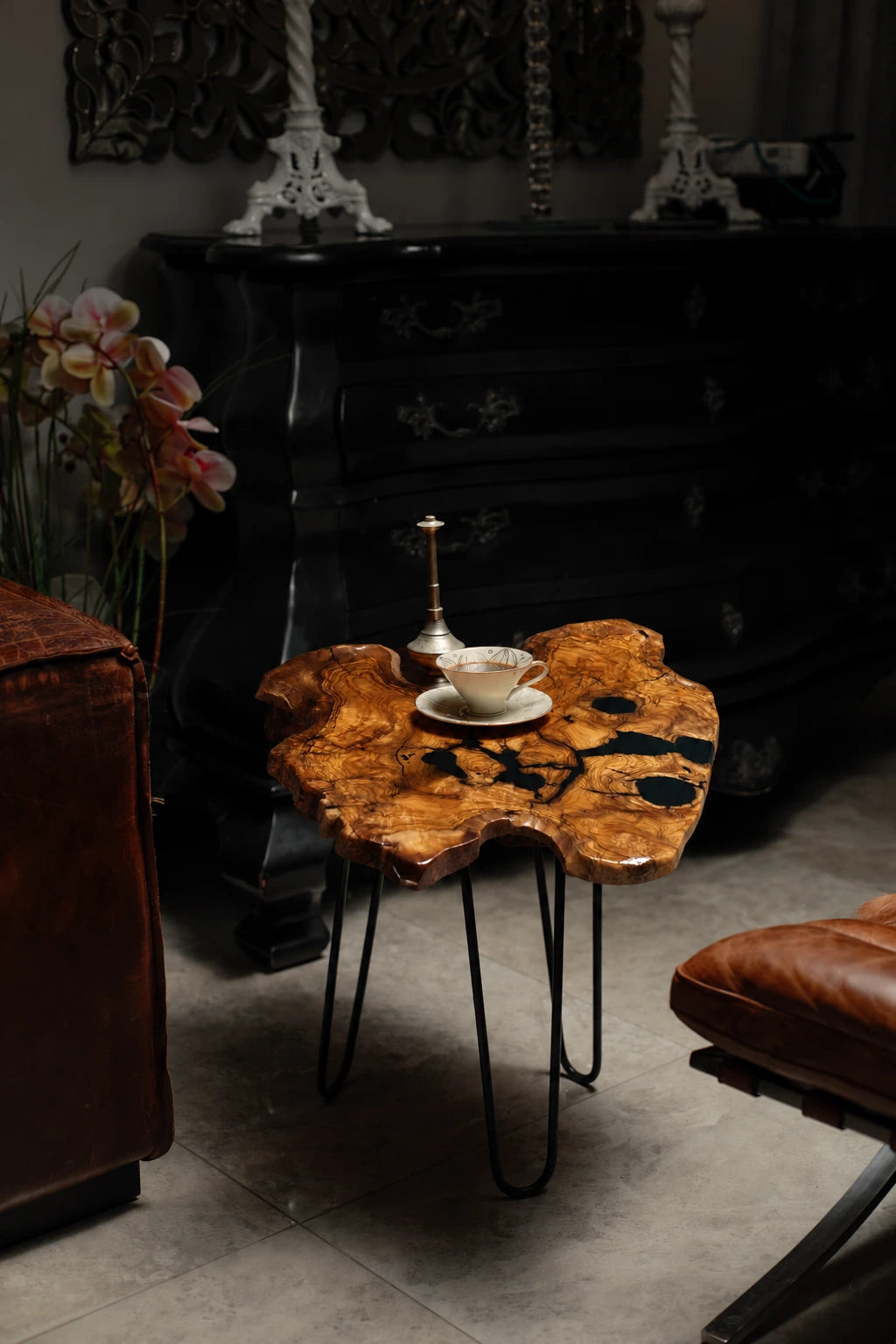 AI-styled view of Zitun Atelier table 049, an olive wood resin small coffee table with black resin spots, in a dark interior beside leather seating.