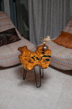 AI-styled view of Zitun Atelier table 049, an olive wood resin small coffee table with black resin spots, viewed from above between two upholstered armchairs.