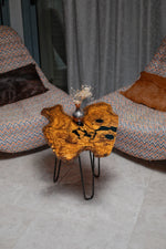AI-styled view of Zitun Atelier table 049, an olive wood resin small coffee table with black resin spots, viewed from above between two upholstered armchairs.