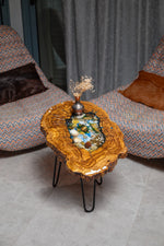 AI-styled view of Zitun Atelier table 052, an olive wood resin side table with sea shell pebble resin, viewed from above between two upholstered armchairs.