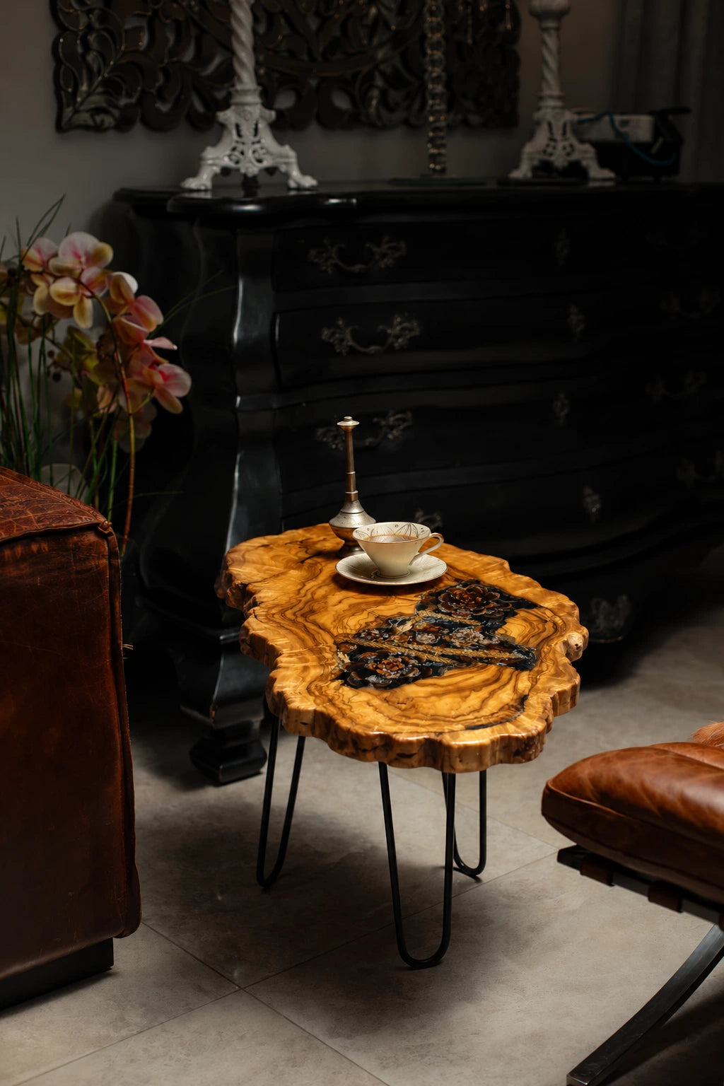 AI-styled view of Zitun Atelier table 053, an olive wood resin side table with pine cone black resin, in a dark interior beside leather seating.