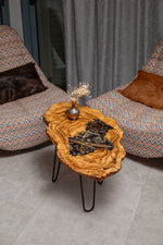 AI-styled view of Zitun Atelier table 053, an olive wood resin side table with pine cone black resin, viewed from above between two upholstered armchairs.