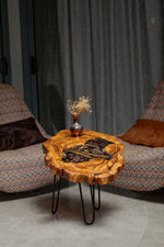 AI-styled view of Zitun Atelier table 053, an olive wood resin side table with pine cone black resin, in a lounge setting with a vase on the tabletop.