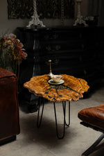 AI-styled view of Zitun Atelier table 055, an olive wood resin small coffee table with black resin clock gears, in a dark interior beside leather seating.