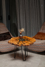 AI-styled view of Zitun Atelier table 055, an olive wood resin small coffee table with black resin clock gears, in a lounge setting with a vase on the tabletop.