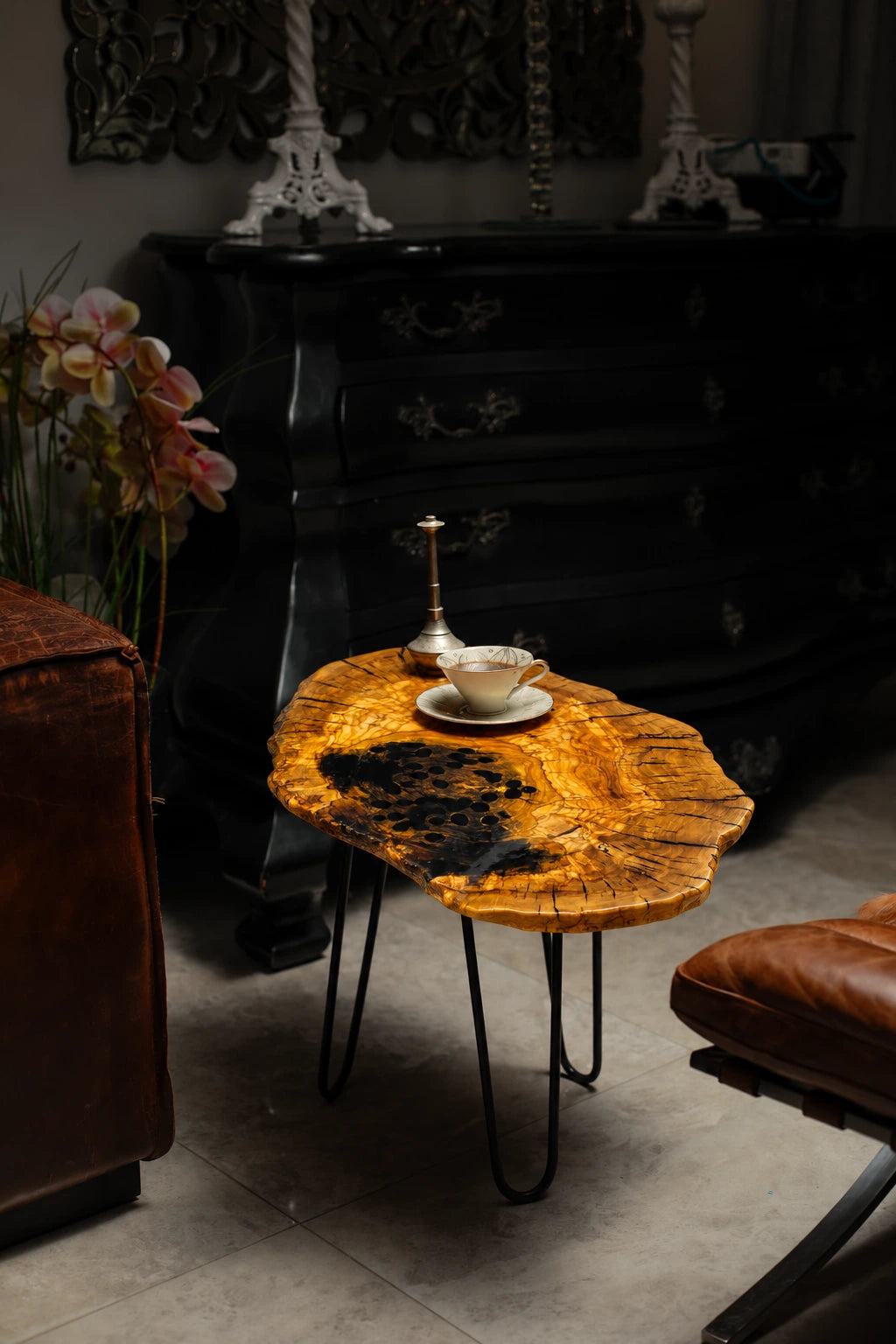 AI-styled view of Zitun Atelier table 056, an olive wood resin side table with black resin, in a dark interior beside leather seating.