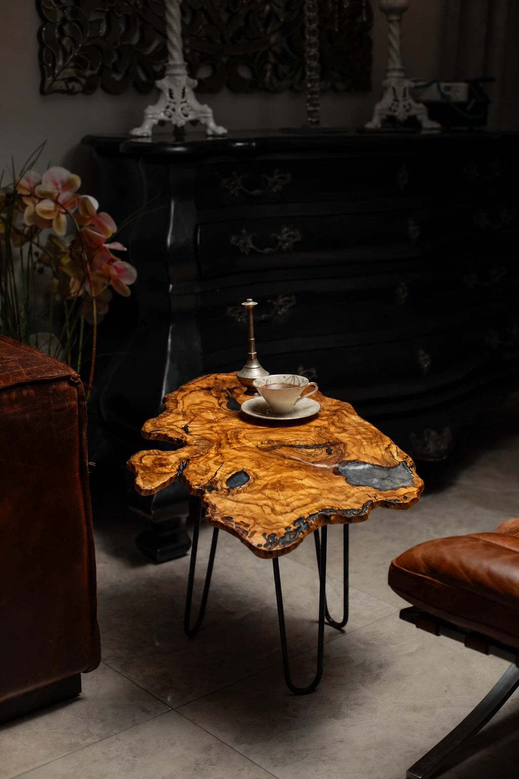 AI-styled view of Zitun Atelier table 062, an olive wood resin side table with blue resin pools, in a dark interior beside leather seating.