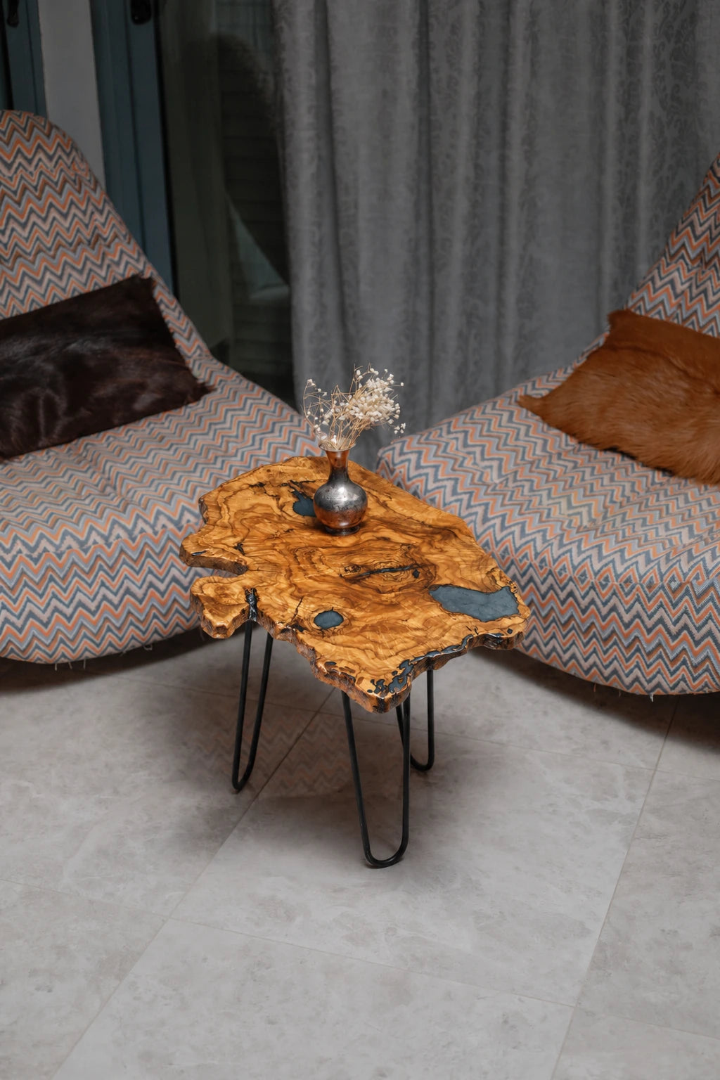 AI-styled view of Zitun Atelier table 062, an olive wood resin side table with blue resin pools, viewed from above between two upholstered armchairs.