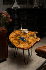 AI-styled view of Zitun Atelier table 064, an olive wood resin side table with metallic blue resin, in a dark interior beside leather seating.