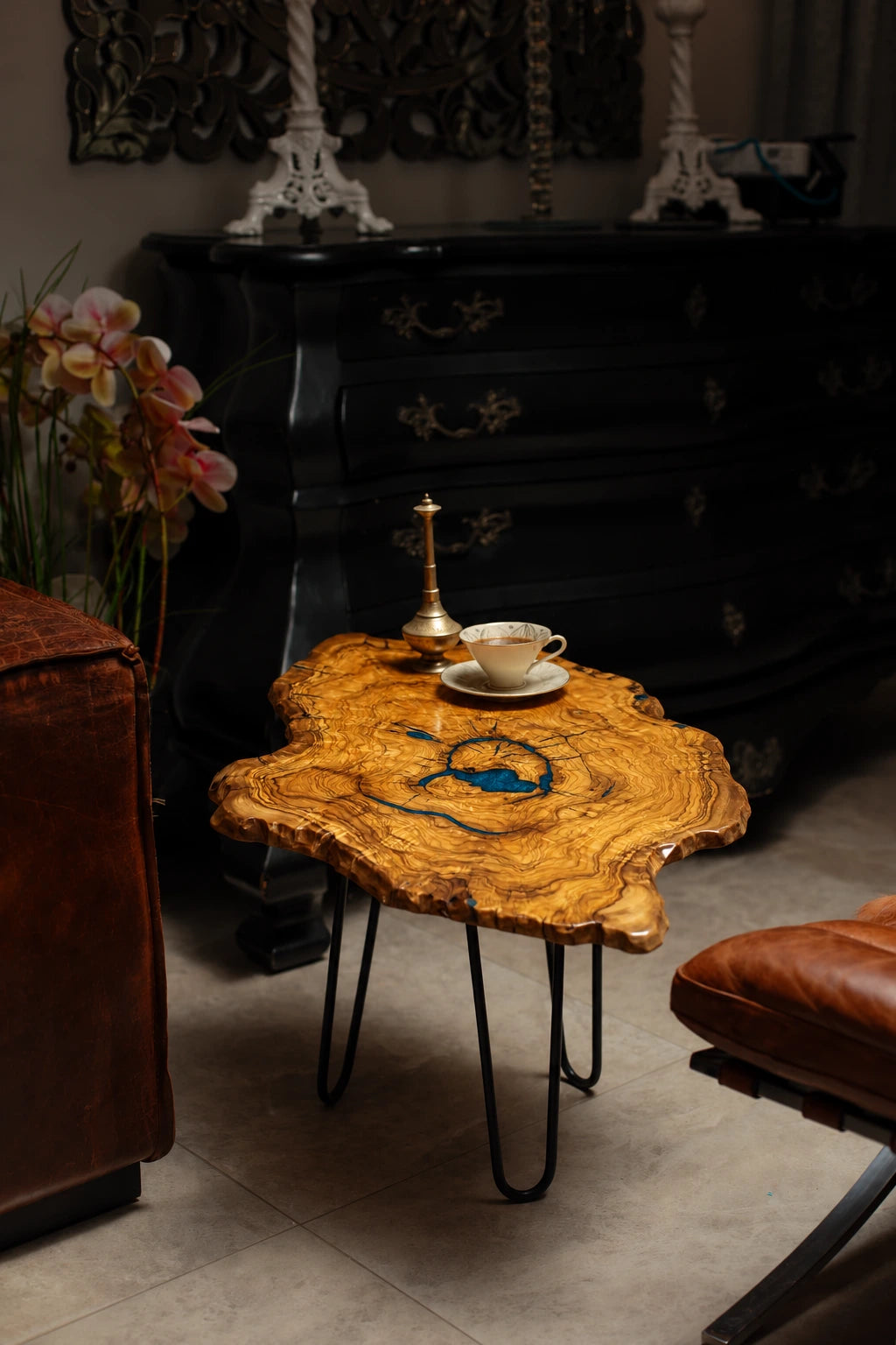 AI-styled view of Zitun Atelier table 065, an olive wood resin side table with blue resin ring, in a dark interior beside leather seating.