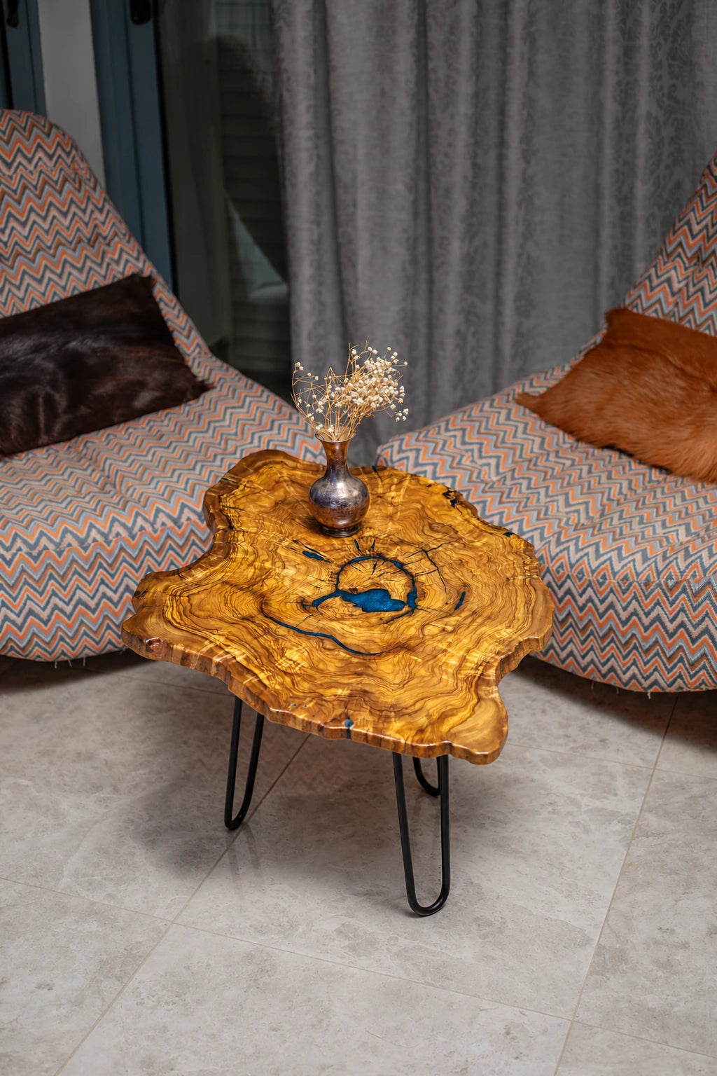 AI-styled view of Zitun Atelier table 065, an olive wood resin side table with blue resin ring, viewed from above between two upholstered armchairs.