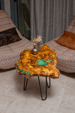 AI-styled view of Zitun Atelier table 067, an olive wood resin side table with turquoise green resin, viewed from above between two upholstered armchairs.