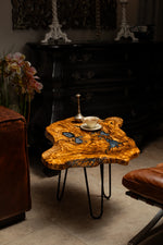 AI-styled view of Zitun Atelier table 073, an olive wood resin small coffee table with blue grey resin, in a dark interior beside leather seating.