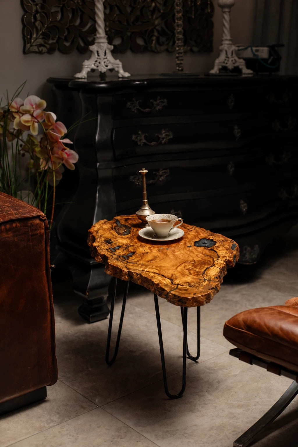 AI-styled view of Zitun Atelier table 077, an olive wood resin side table with black resin knots, in a dark interior beside leather seating.