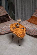 AI-styled view of Zitun Atelier table 077, an olive wood resin side table with black resin knots, viewed from above between two upholstered armchairs.
