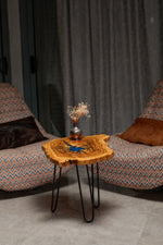 AI-styled view of Zitun Atelier table 079, an olive wood resin side table with blue starburst resin, in a lounge setting with a vase on the tabletop.