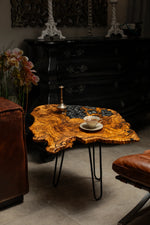 AI-styled view of Zitun Atelier table 080, an olive wood resin side table with black floral resin, in a dark interior beside leather seating.