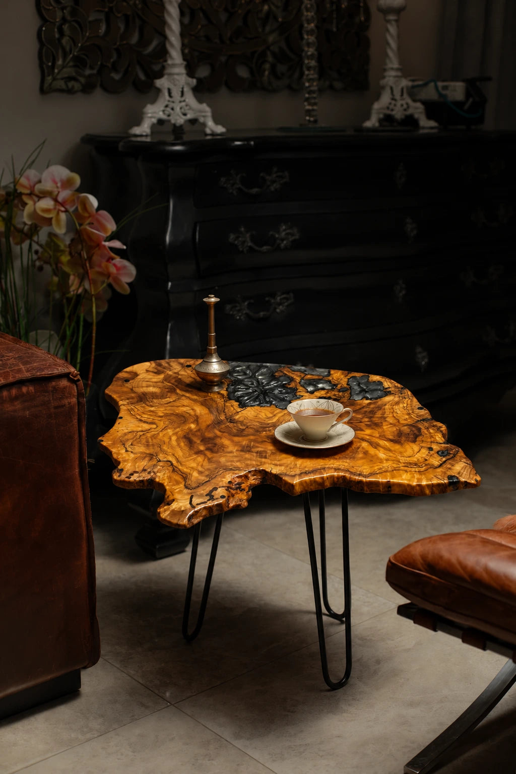 AI-styled view of Zitun Atelier table 080, an olive wood resin side table with black floral resin, in a dark interior beside leather seating.
