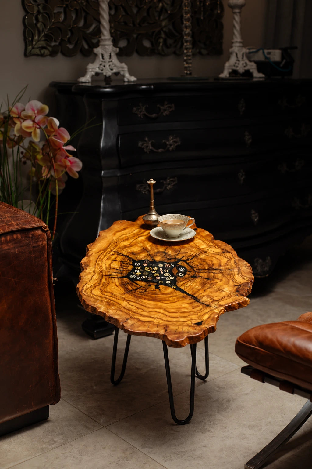 AI-styled view of Zitun Atelier table 083, an olive wood resin side table with black resin steampunk gears, in a dark interior beside leather seating.