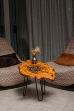 AI-styled view of Zitun Atelier table 083, an olive wood resin side table with black resin steampunk gears, in a lounge setting with a vase on the tabletop.