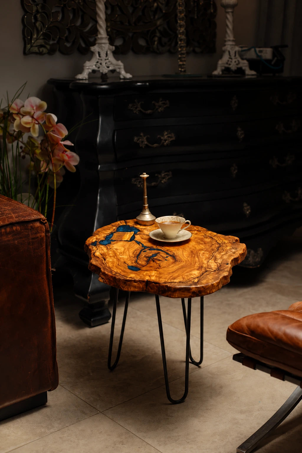 AI-styled view of Zitun Atelier table 087, an olive wood resin side table with blue grey resin veins, in a dark interior beside leather seating.