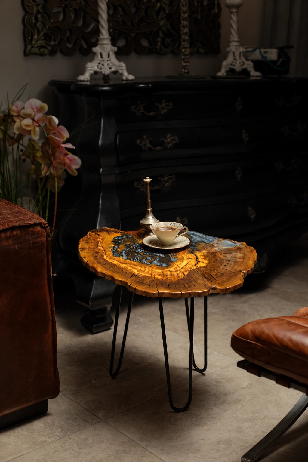 AI-styled view of Zitun Atelier table 092, an olive wood resin side table with black pebble resin, in a dark interior beside leather seating.