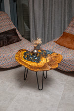AI-styled view of Zitun Atelier table 092, an olive wood resin side table with black pebble resin, viewed from above between two upholstered armchairs.