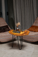 AI-styled view of Zitun Atelier table 092, an olive wood resin side table with black pebble resin, in a lounge setting with a vase on the tabletop.