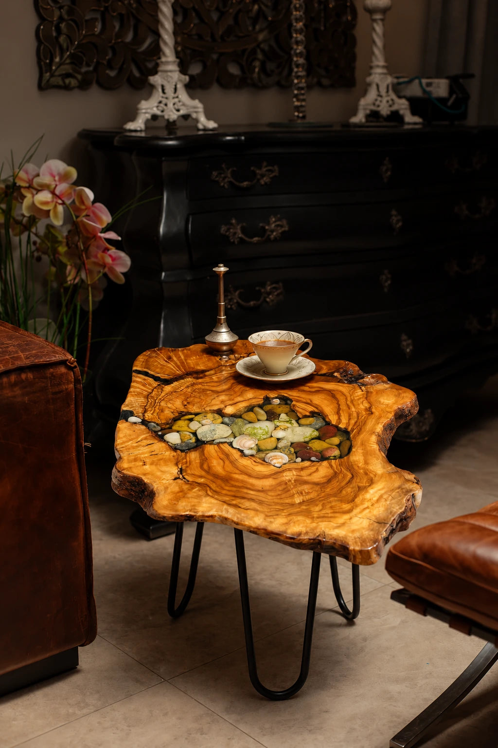 AI-styled view of Zitun Atelier table 093, an olive wood resin side table with sea shell pebble resin, in a dark interior beside leather seating.