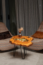 AI-styled view of Zitun Atelier table 093, an olive wood resin side table with sea shell pebble resin, in a lounge setting with a vase on the tabletop.