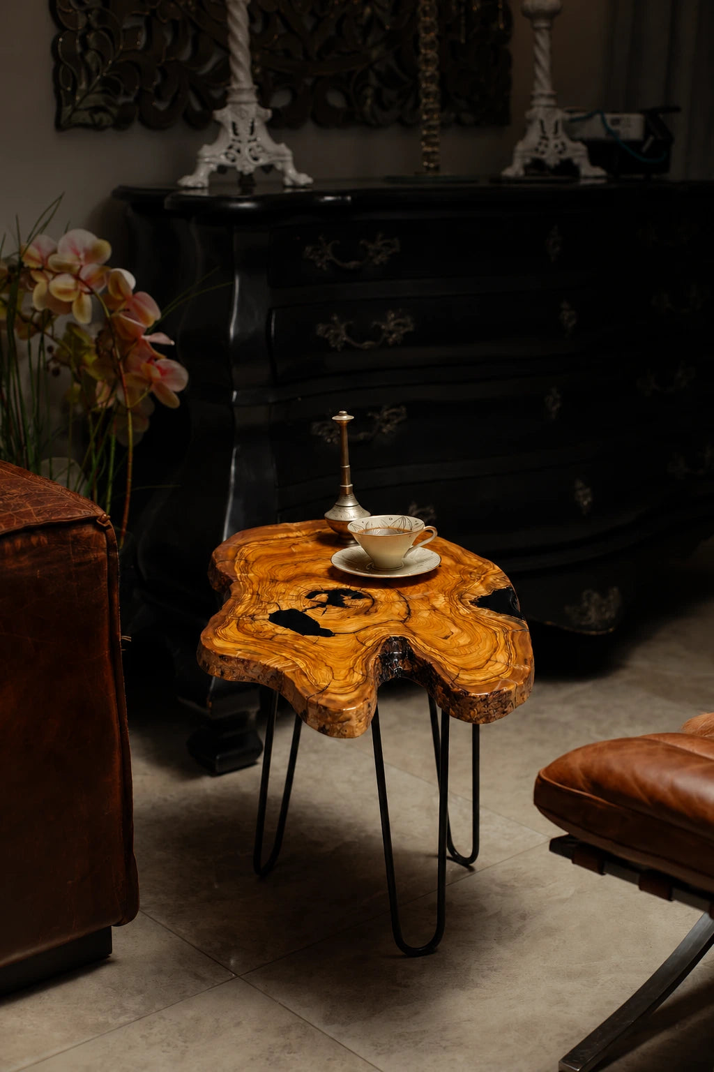 AI-styled view of Zitun Atelier table 094, an olive wood resin side table with black resin inlay, in a dark interior beside leather seating.