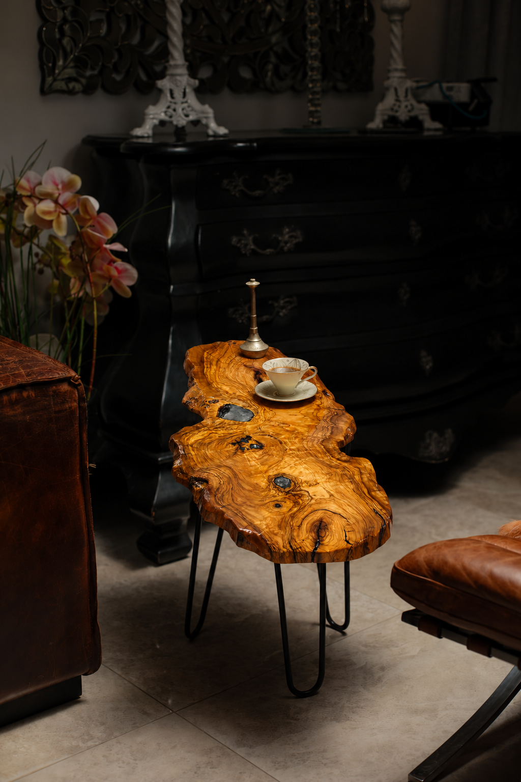 AI-styled view of Zitun Atelier table 099, an olive wood resin small coffee table with black resin knots, in a dark interior beside leather seating.