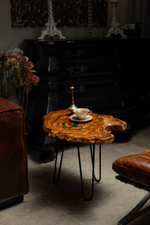 AI-styled view of Zitun Atelier table 002, a live-edge olive wood side table with teal resin, beside leather seating in a dark interior.